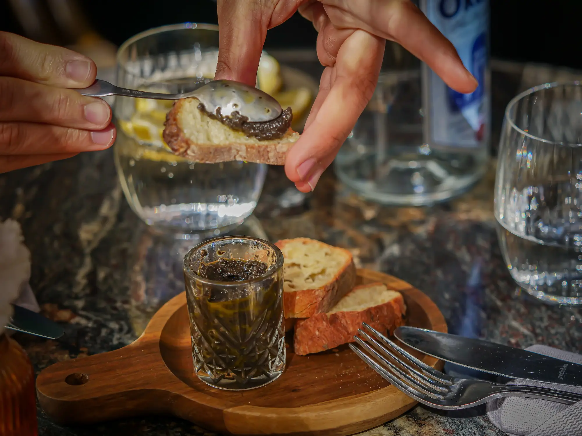 Tartare d'olives servi en verre avec tranches de pain grillé sur planche en bois